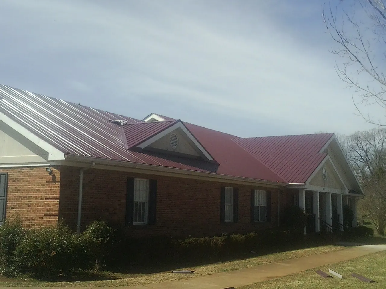 Red metal roof with gabled entries on a long brick building, from a Hail Damage Roof Repair job in Rickreall