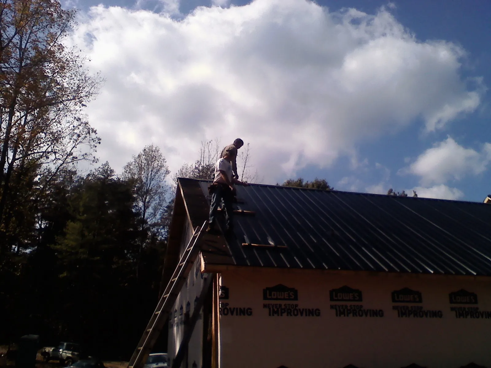 Roofer fastening dark metal panels high against a cloudy sky, from a Roof Inspection job in Rickreall