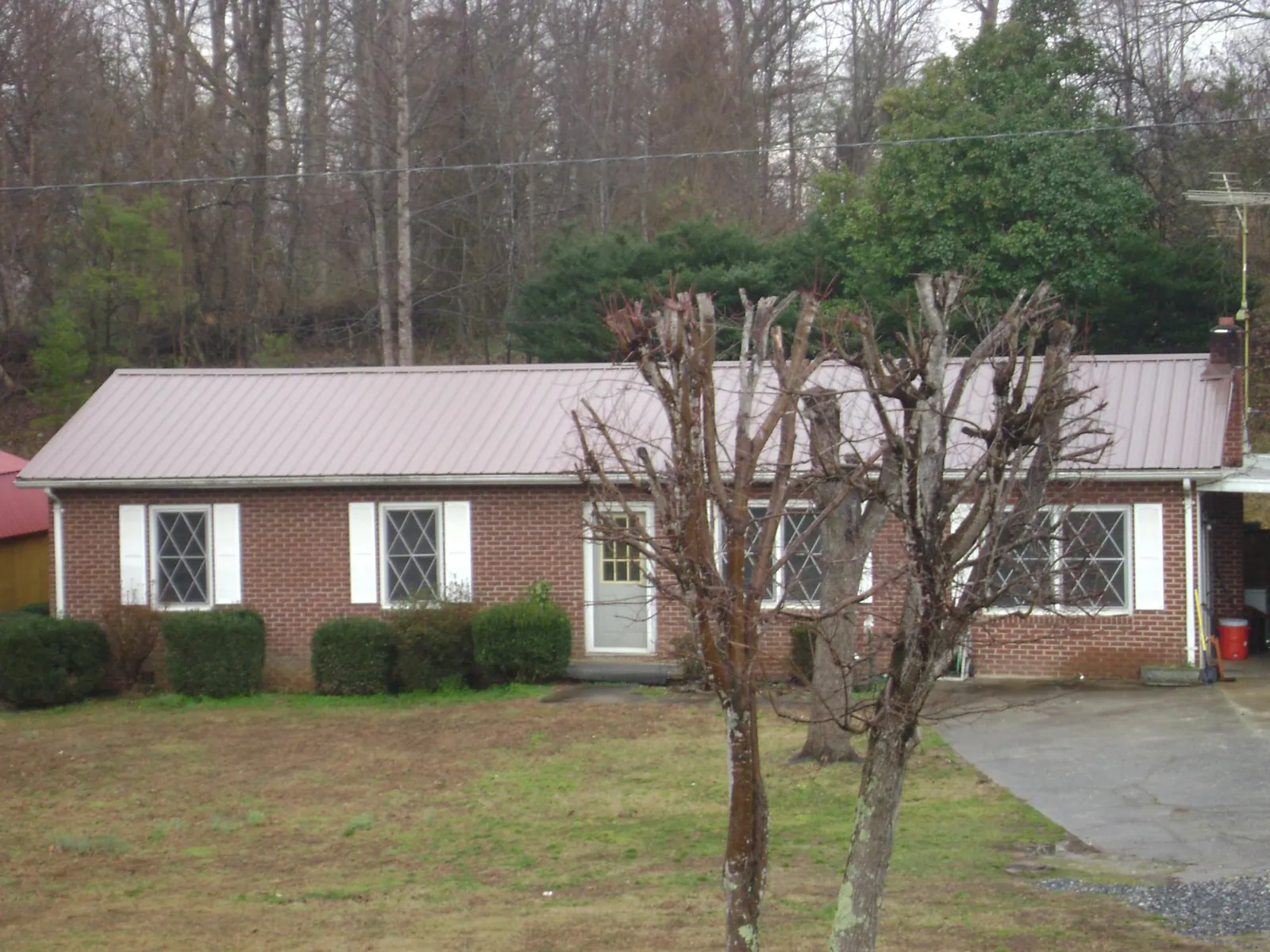 Mauve metal roof on a brick ranch home behind bare trees in Rickreall