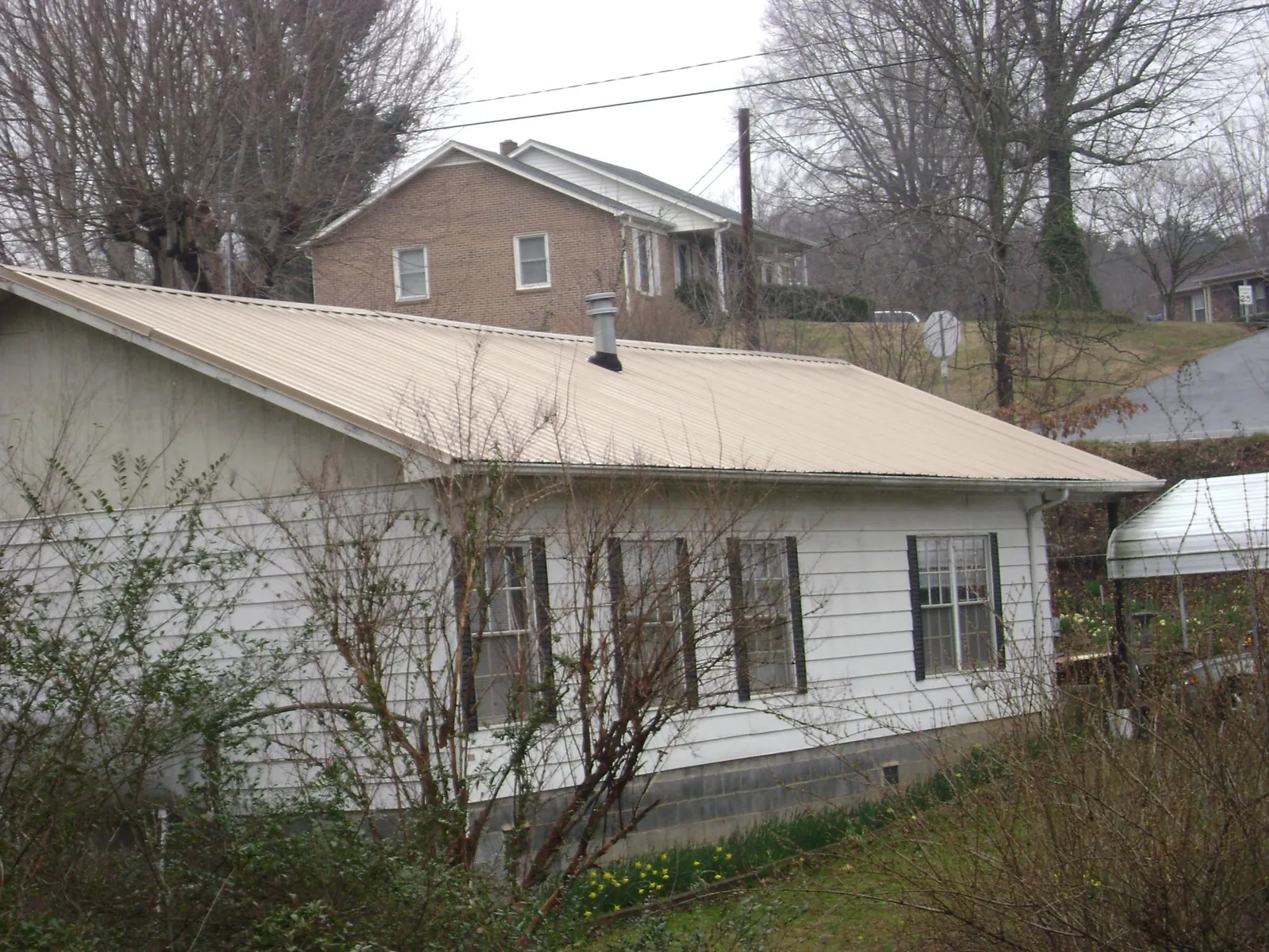 Tan metal roof on a white sided house set into a hillside — Commercial Roofing by Roofing Brothers in Rickreall